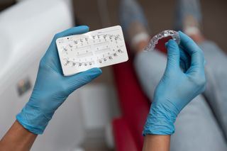 Gloved hands holding a clear aligner next to a dental model